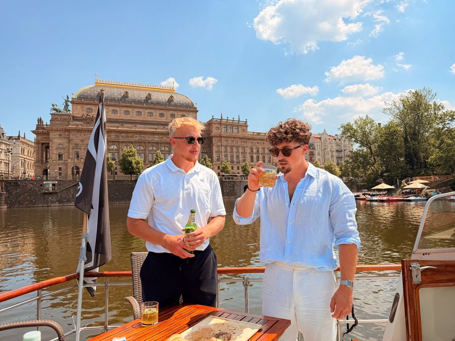 Friends with drinks on a private river experience in Prague, National Theatre behind